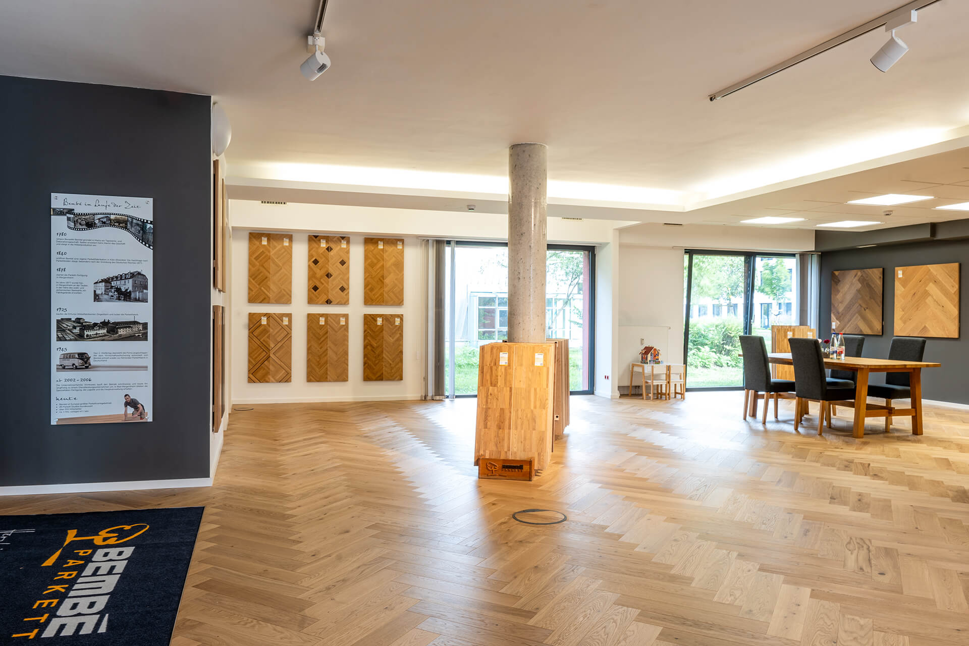 Heller Showroom mit Parkettmustern an den Wänden, Tisch und Stühlen in der Mitte, umgeben von großen Fenstern