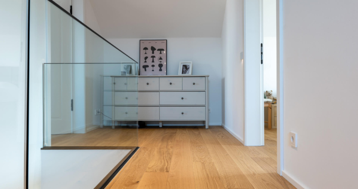 comfort-tabis-diele-eiche-standard-geölt-4 Eichenholz-Landhausdiele im Flur mit gläsernem Treppengeländer und Kommode im Dachgeschoss bei Heilbronn
