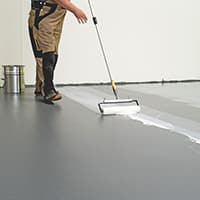 Arbeiter trägt elastischen Bodenbelag auf Betonuntergrund auf